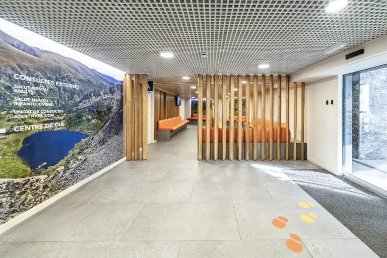 Vestíbul d'entrada del Centre Comunitari de Salut Mental i Addiccions del SAAS amb mural fotogràfic d'un llac d'Andorra i separadors de llistons de fusta